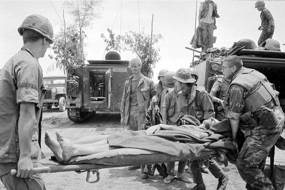 Navy SEAL Lieutenant Tom Norris observes as medical personnel carry LTCOL Hambleton to a waiting armored personnel carrier. (USAF)